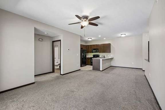 A spacious living room with a ceiling fan and carpeted floor.