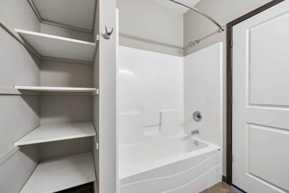A white bathroom with a tub and shelves.