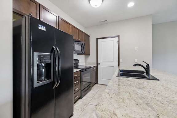 A black refrigerator is in a kitchen with granite countertops.