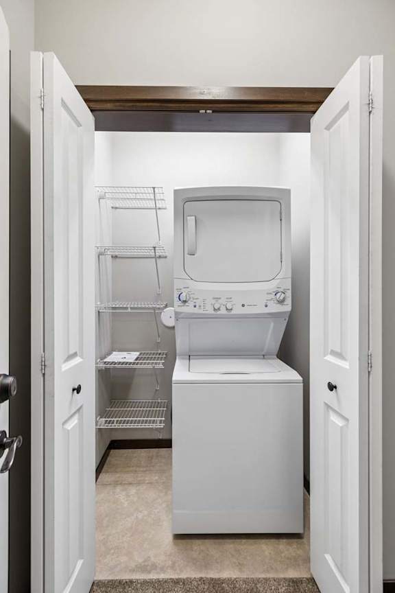Laundry closet with stacked washer and dryer, white wire shelving, and tile flooring.