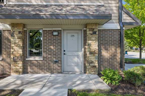 Apartment exterior entry with brick facade, stone columns, unit door 175, sidewalk, and landscaped greenery.