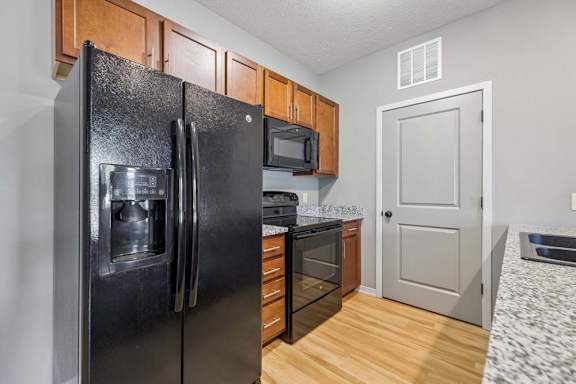 Open apartment kitchen with breakfast bar, speckled countertops, black appliances, and wood-look flooring.