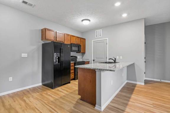 Apartment kitchen with wood cabinets, speckled counters, black appliances, and wood-look flooring.