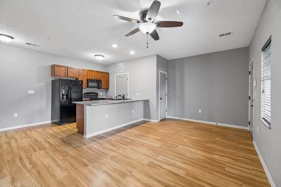 Open apartment kitchen with breakfast bar, speckled countertops, black appliances, and wood-look flooring.