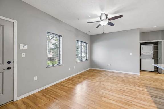 Bright apartment living room with wood-look flooring, ceiling fan, gray walls, and large windows with blinds.