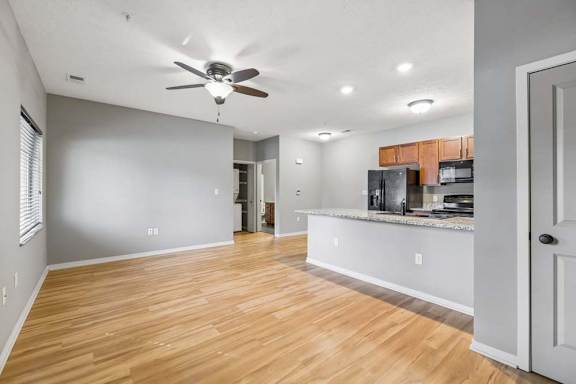 Spacious apartment living area with wood-look flooring, ceiling fan, gray walls, and kitchen breakfast bar.