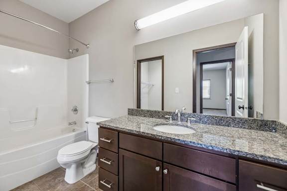 Apartment bathroom with granite-style vanity, dark cabinets, large mirror, toilet, and glass-door shower.