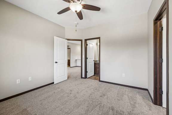 Carpeted apartment bedroom with ceiling fan, gray walls, dark trim, and open doors to the bathroom and living area.