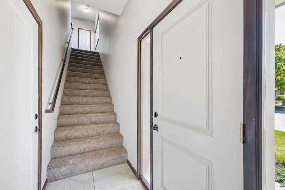 Apartment entryway with tiled floor, carpeted stairs, dark trim, interior doors, and front door with sidelight window.