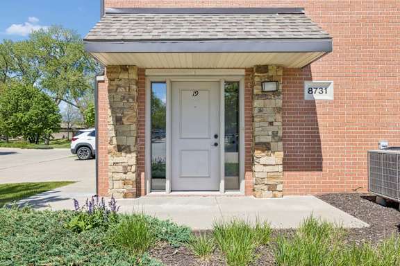 Apartment entry with brick exterior, stone columns, covered doorway, landscaping, and visible unit number 19.