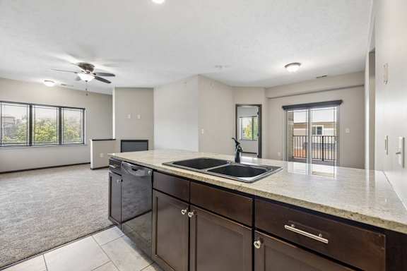 Open apartment kitchen with granite-style countertops, dark cabinets, double sink, and view into living room with balcony access.