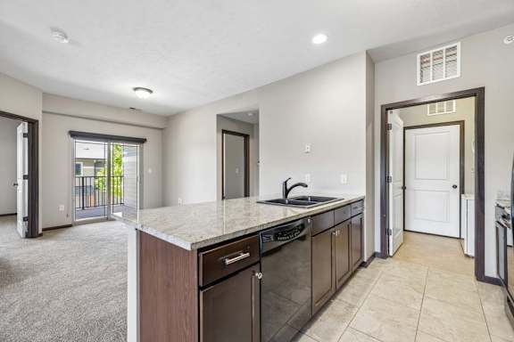 Open apartment kitchen with granite-style island, dark cabinets, black dishwasher, tile flooring, and balcony access.