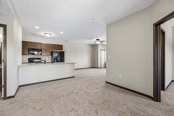 Open apartment living area with carpet, dark trim, ceiling fan, and kitchen with breakfast bar and black appliances.