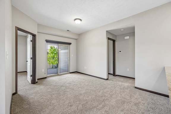 Carpeted apartment living room with gray walls, dark trim, sliding glass doors, and access to a private balcony.