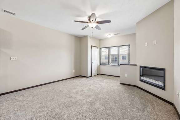 Carpeted apartment living room with ceiling fan, large window, dark trim, and wall fireplace.