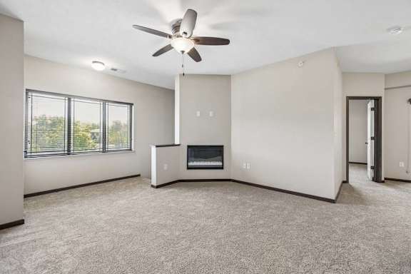 Carpeted apartment living room with ceiling fan, large windows, dark trim, and a built-in fireplace.