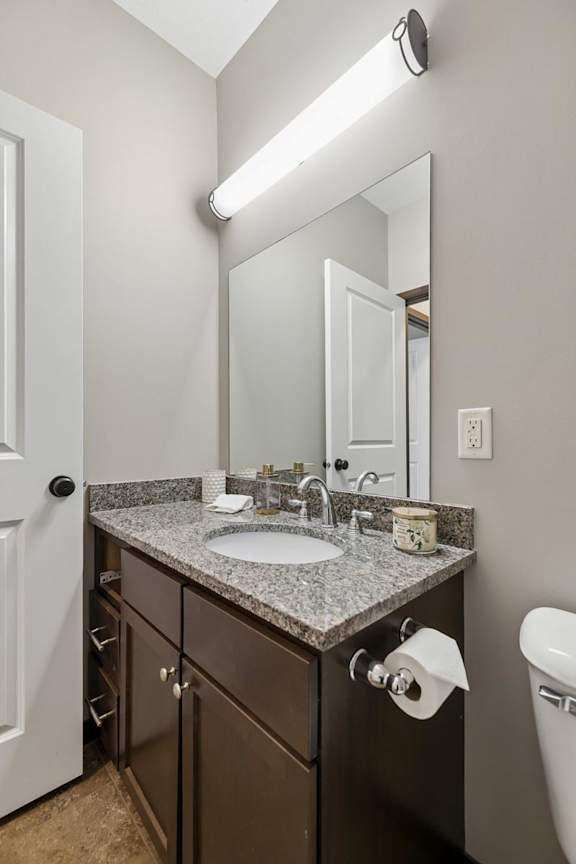 Staged apartment bathroom vanity with speckled countertop, dark wood cabinets, large mirror, and tile flooring.