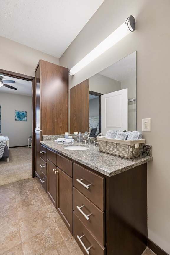 Staged apartment bathroom vanity with speckled countertop, dark wood cabinets, large mirror, and tile flooring.