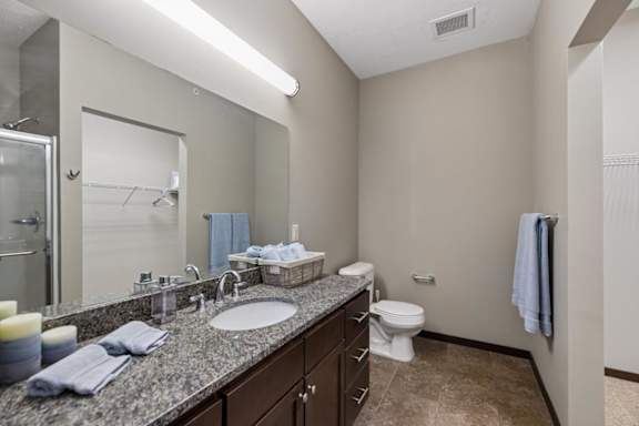 Apartment bathroom with speckled vanity, dark wood cabinetry, large mirror, tile floor, and walk-in closet access.