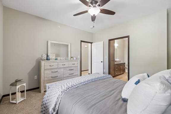 Staged apartment bedroom with ceiling fan, dresser, carpet, and direct access to the bathroom.