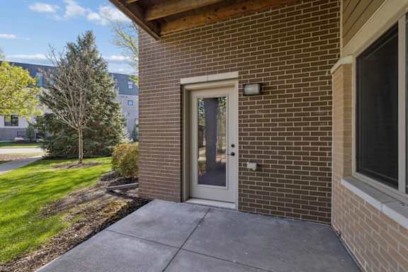 Covered apartment patio with brick wall, glass door, concrete slab, and landscaped grounds.
