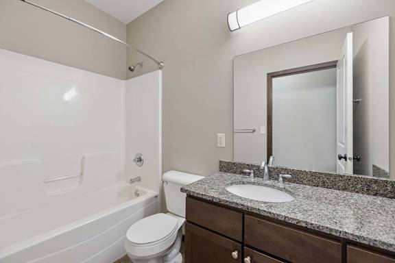 A bathroom with a white toilet, a white bathtub, and a sink with a mirror above it.