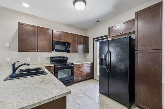 A kitchen with a black refrigerator and brown cabinets.