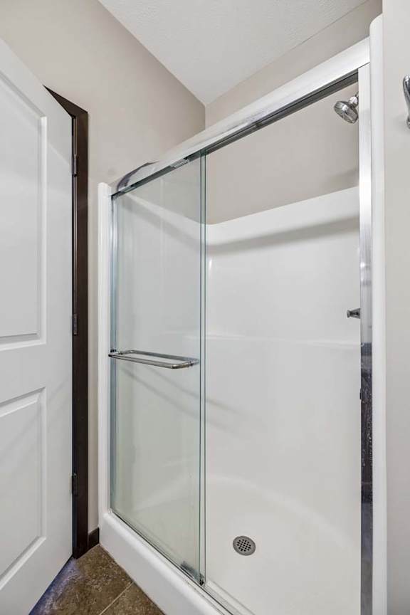 A white shower stall with a glass door is open to a white bathroom.