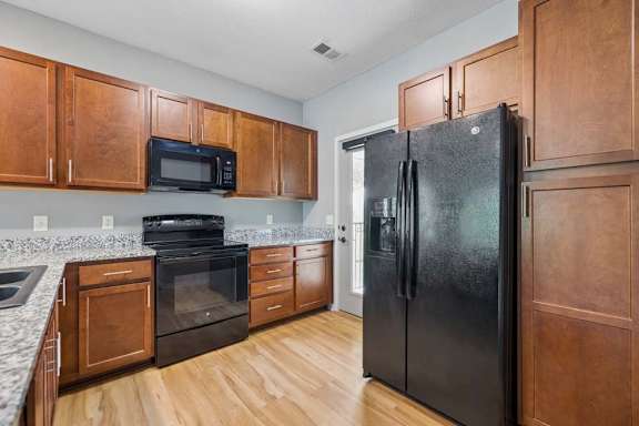 A black refrigerator is in a kitchen with wooden cabinets.