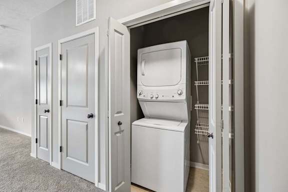 A white stackable washing machine is in a small closet.