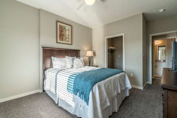 A bedroom with a bed, a ceiling fan, and a painting on the wall.