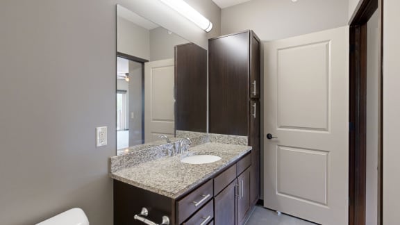 a bathroom vanity with large mirror, light granite countertops, and dark cabinets