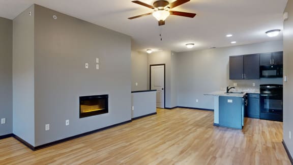 an empty living room with a fireplace and kitchen in the background