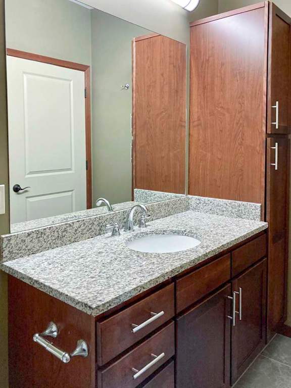 A bathroom with a granite vanity sink, large mirror, and tall storage cabinet.
