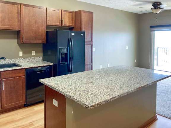 A kitchen with granite countertops, wooden cabinets, black appliances, and a large central island.