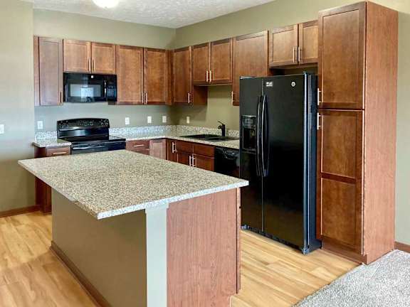 A kitchen with granite countertops, wooden cabinets, black appliances, and a large central island.