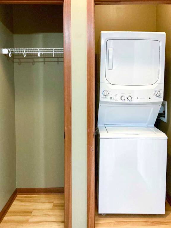 A white stacked washer and dryer in a closet, next to another closet with a shelf.
