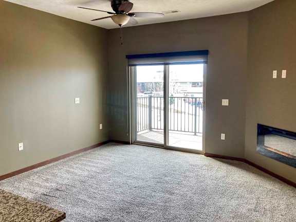 A living room with a ceiling fan, sliding glass door to a balcony, and electric fireplace.