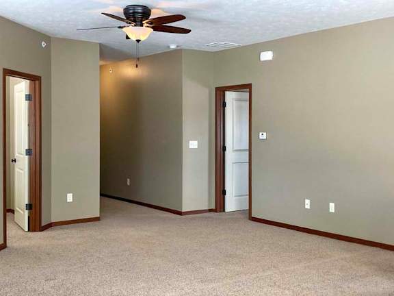 A living room with a ceiling fan and doors to the bedroom and den space.