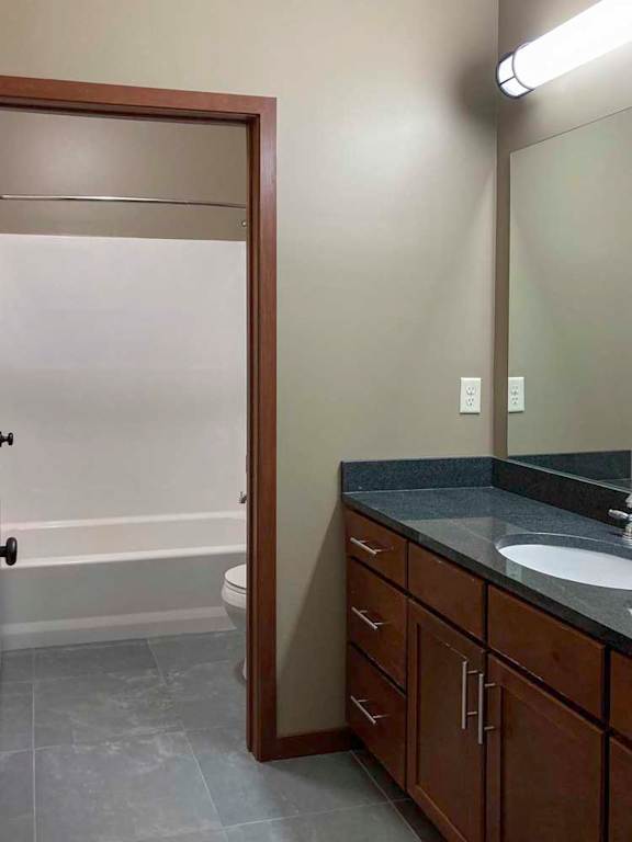 A hallway bathroom with a granite vanity sink, oversized mirror, and a private shower room.