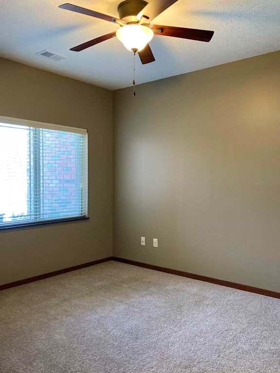 A carpeted bedroom with a ceiling fan, and a large window with blinds.
