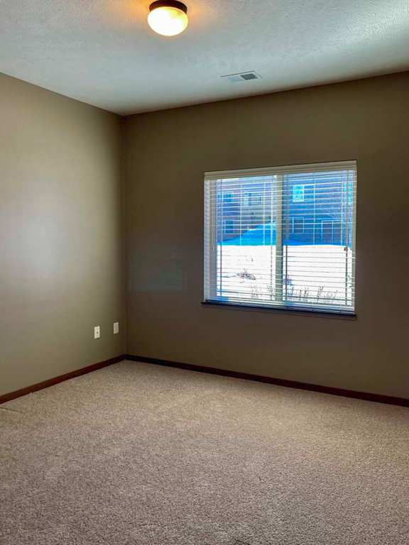 A carpeted bedroom with a large window and blinds.