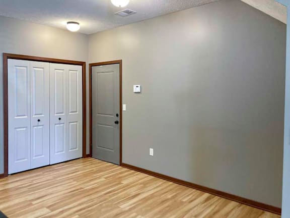 A living area with hardwood-style flooring, a double door closet, and a door to an attached garage.