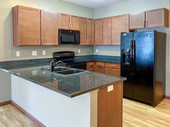 A modern kitchen with brown cabinets, dark granite counters, a peninsula, and black appliances.
