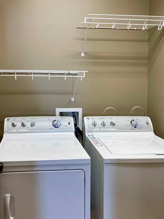 A laundry room with a full-sized side-by-side washer and dryer, with overhead shelving.