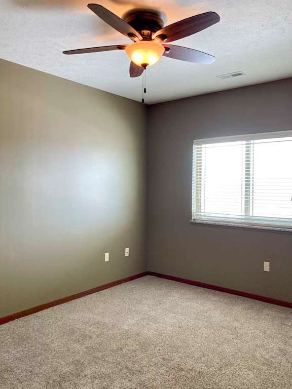 A carpeted bedroom with a ceiling fan, and a large window with blinds.
