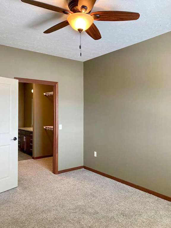 A carpeted bedroom with a ceiling fan and attached walk-in closet and bathroom suite.