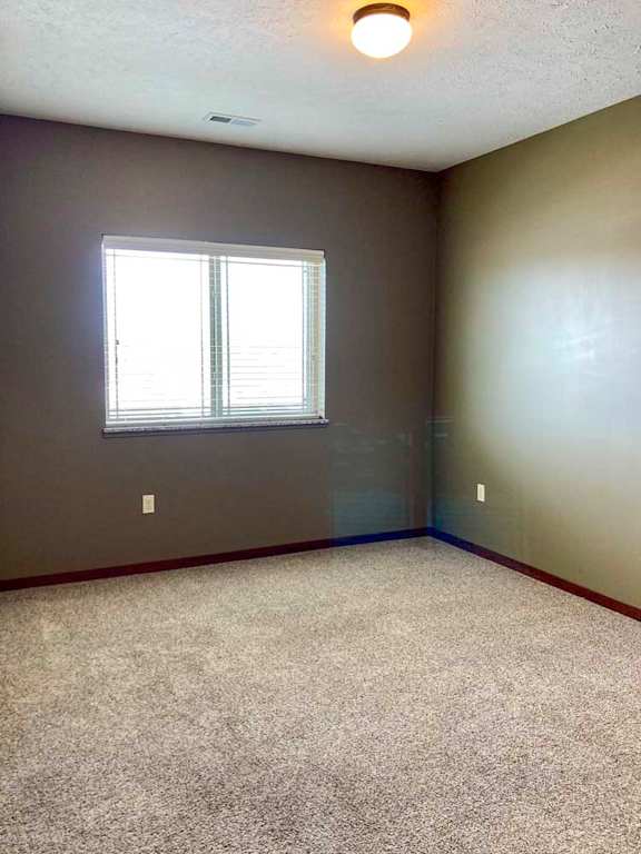 A carpeted bedroom with a large window and blinds.