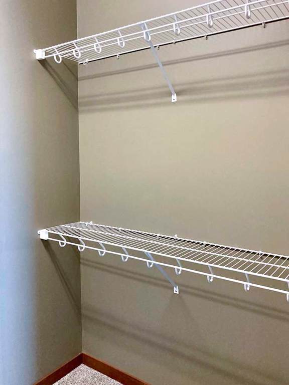 A walk-in closet with two wide wire shelves for hanging space.