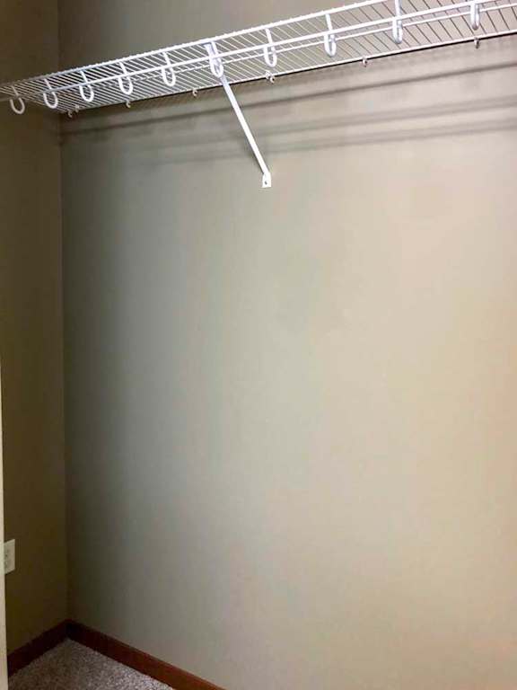 A walk-in closet with an overhead wire shelf for hanging space.
